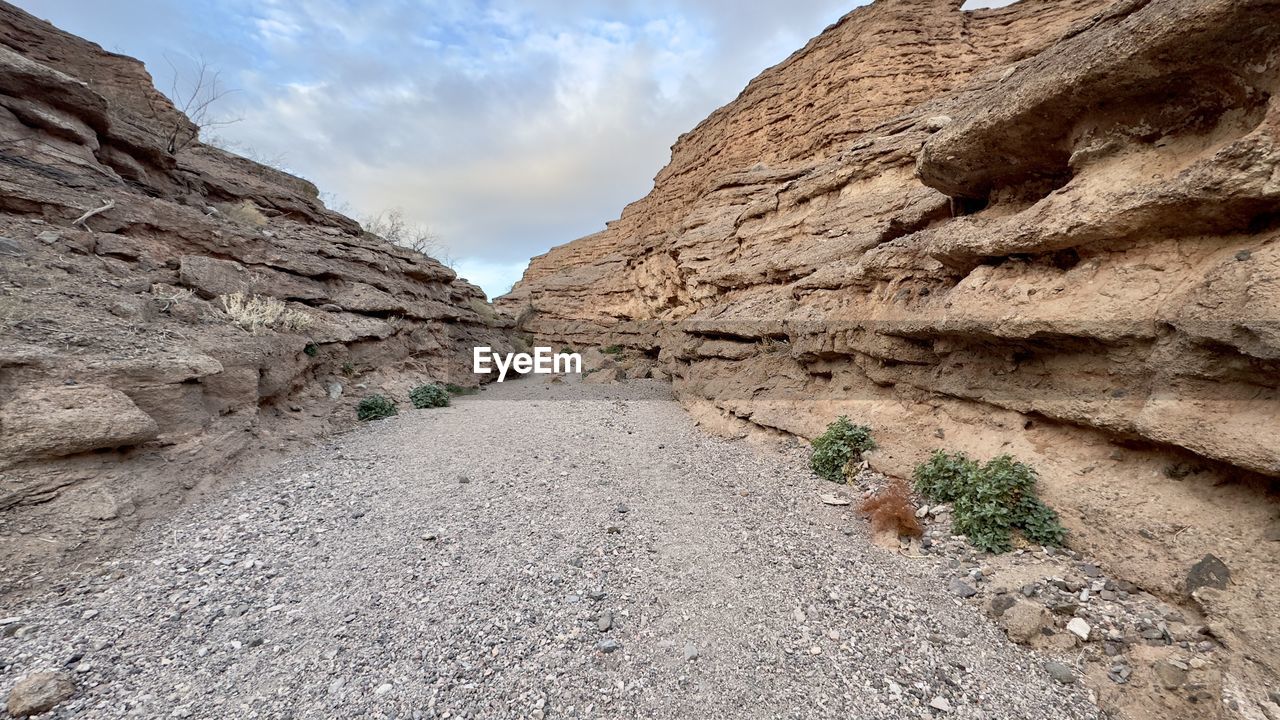 landscape, rock, sky, environment, wadi, scenics - nature, nature, cloud, valley, beauty in nature, land, geology, rock formation, mountain, travel destinations, desert, travel, non-urban scene, no people, terrain, outdoors, tranquility, cliff, extreme terrain, mountain range, arid climate, day, climate, plant, road, wilderness, tranquil scene, tourism, physical geography, soil, canyon, semi-arid, footpath, plateau, activity, accidents and disasters