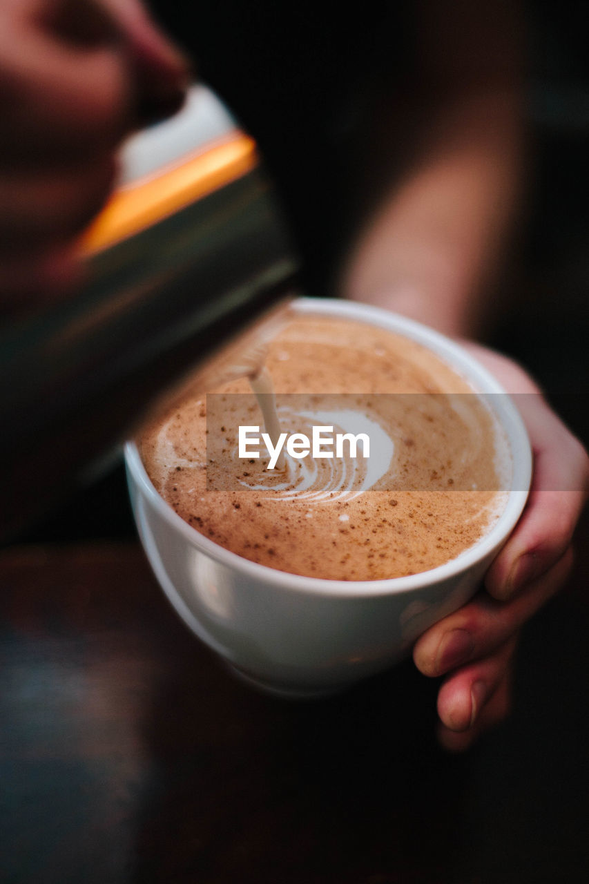 Close-up of hand pouring cream in coffee cup