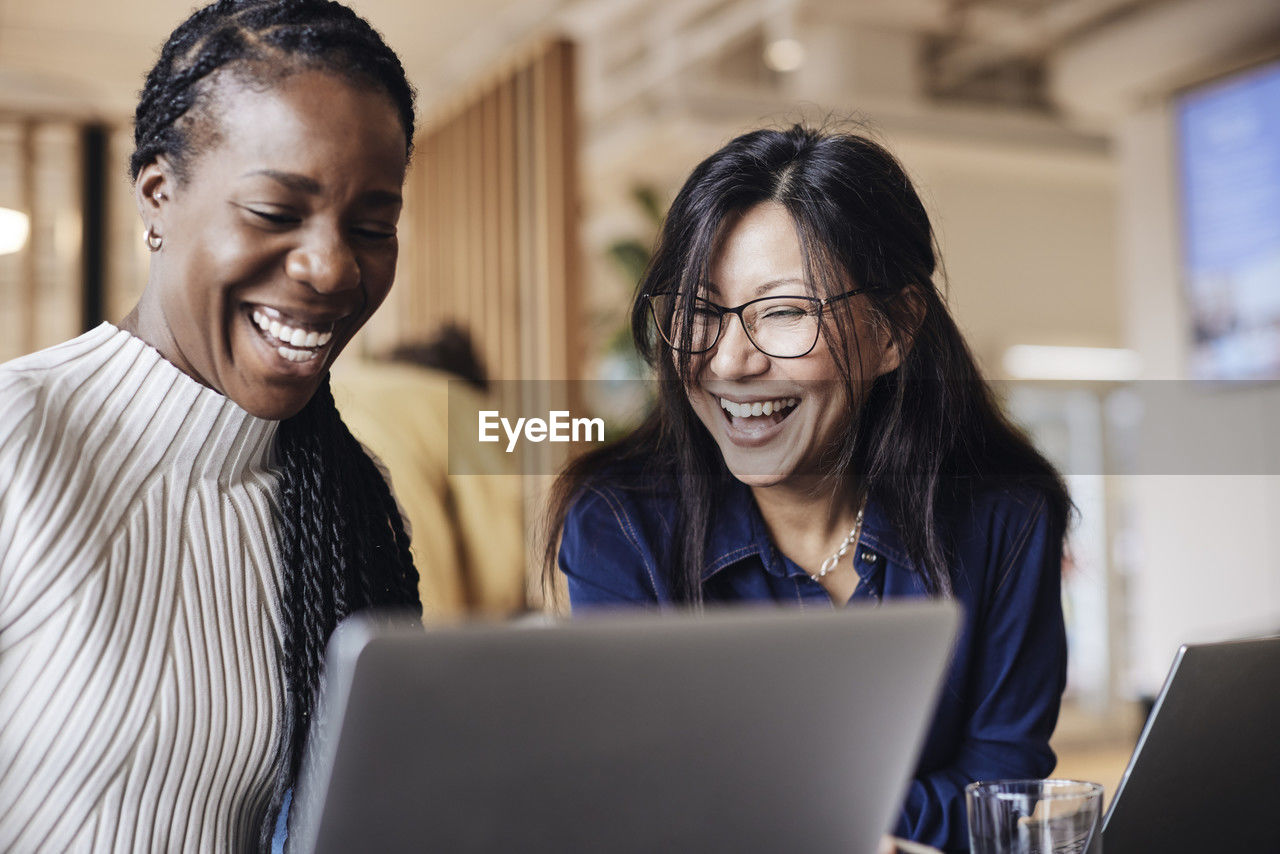 Happy female business professionals sharing laptop at coworking office