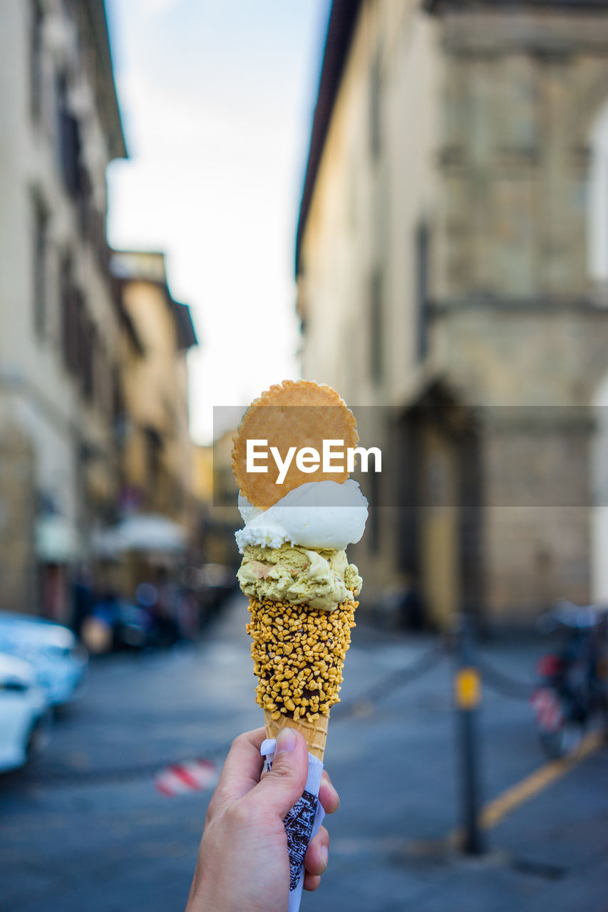 Cropped hand holding ice cream against buildings in city