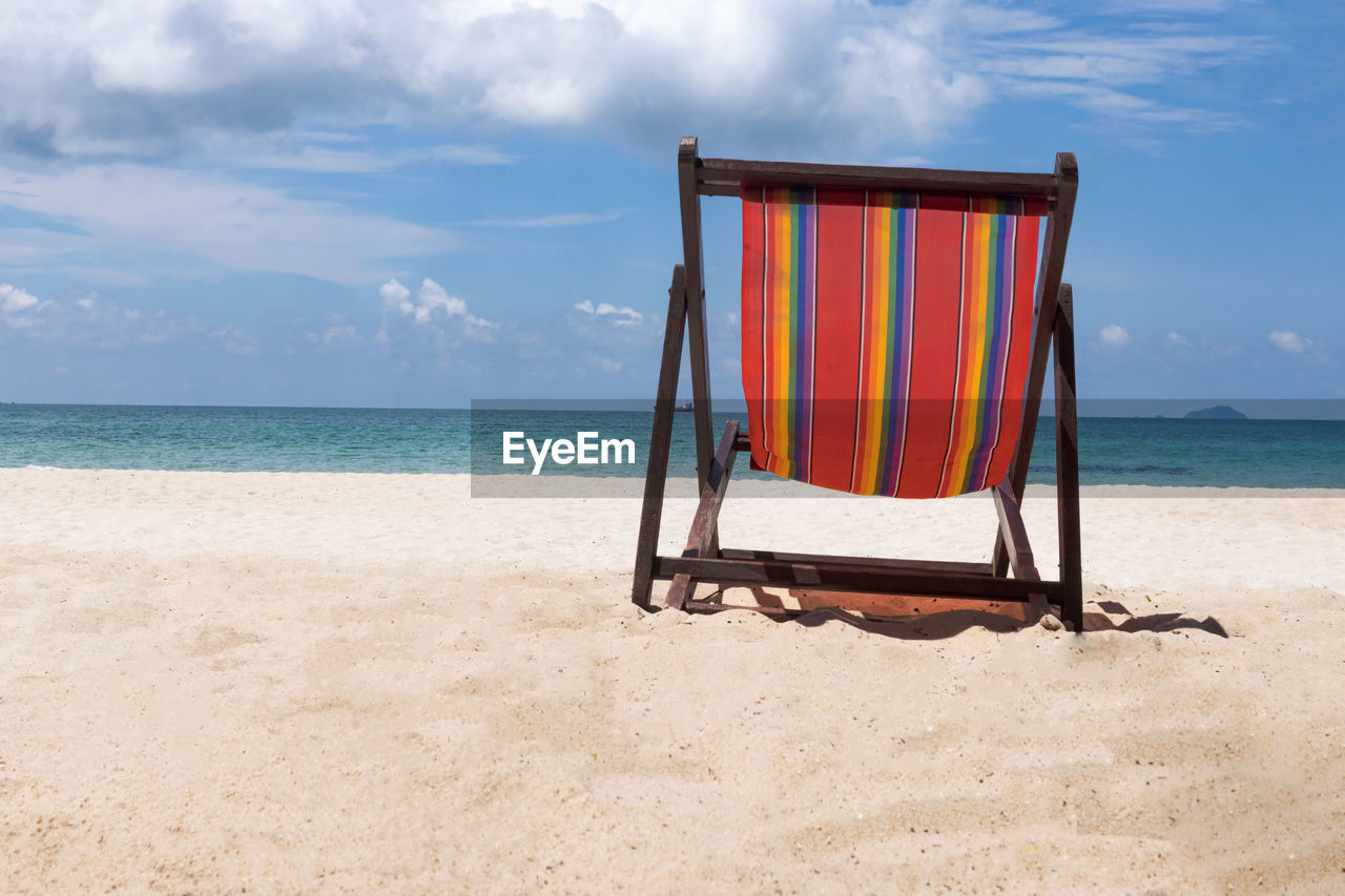 LOUNGE CHAIRS ON BEACH AGAINST SKY