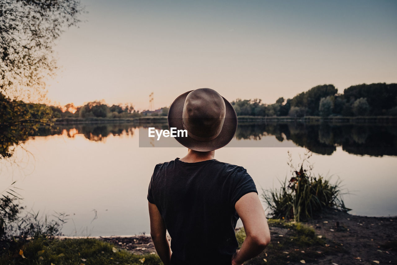 Rear view of young woman looking at lake against sky during sunset