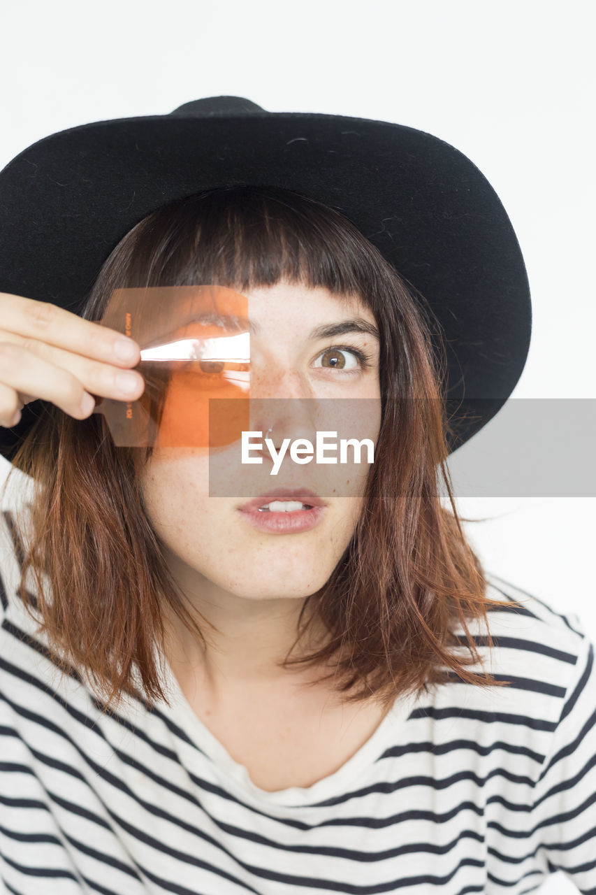 Portrait of young woman looking through orange plastic against white background