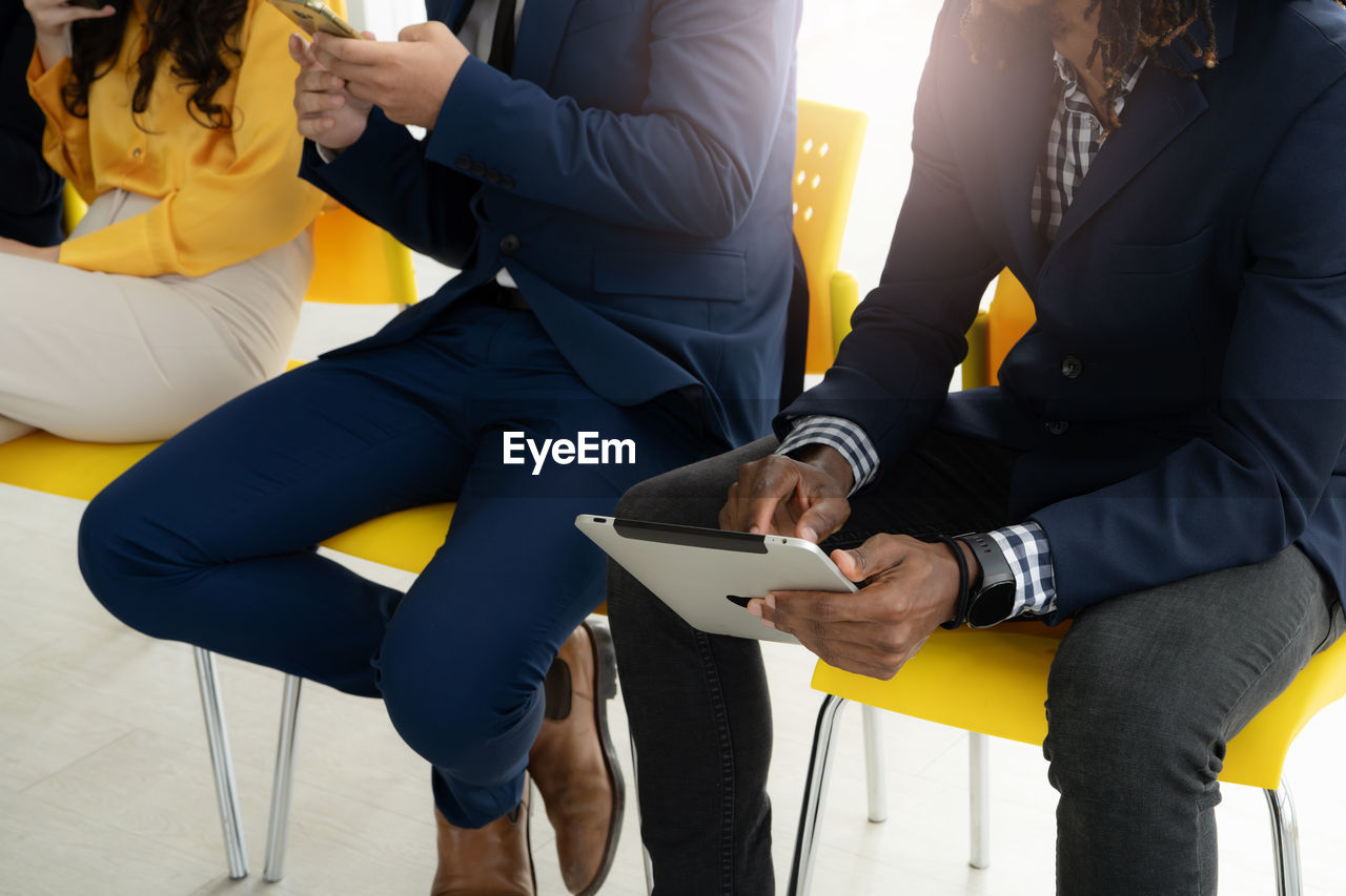 Two men in suits are sitting in chairs, one of them holding a tablet. concept of professionalism