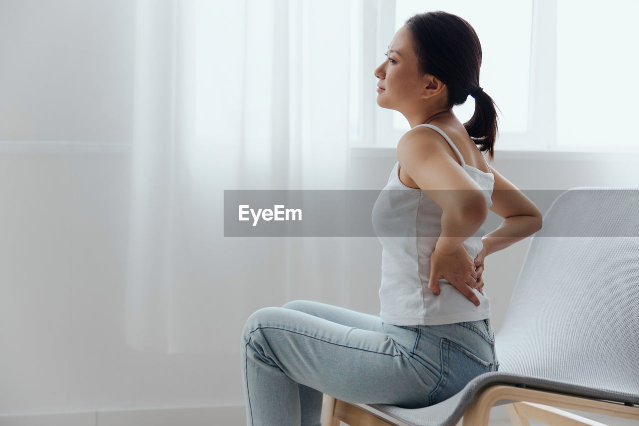 Young woman with back pain sitting on chair