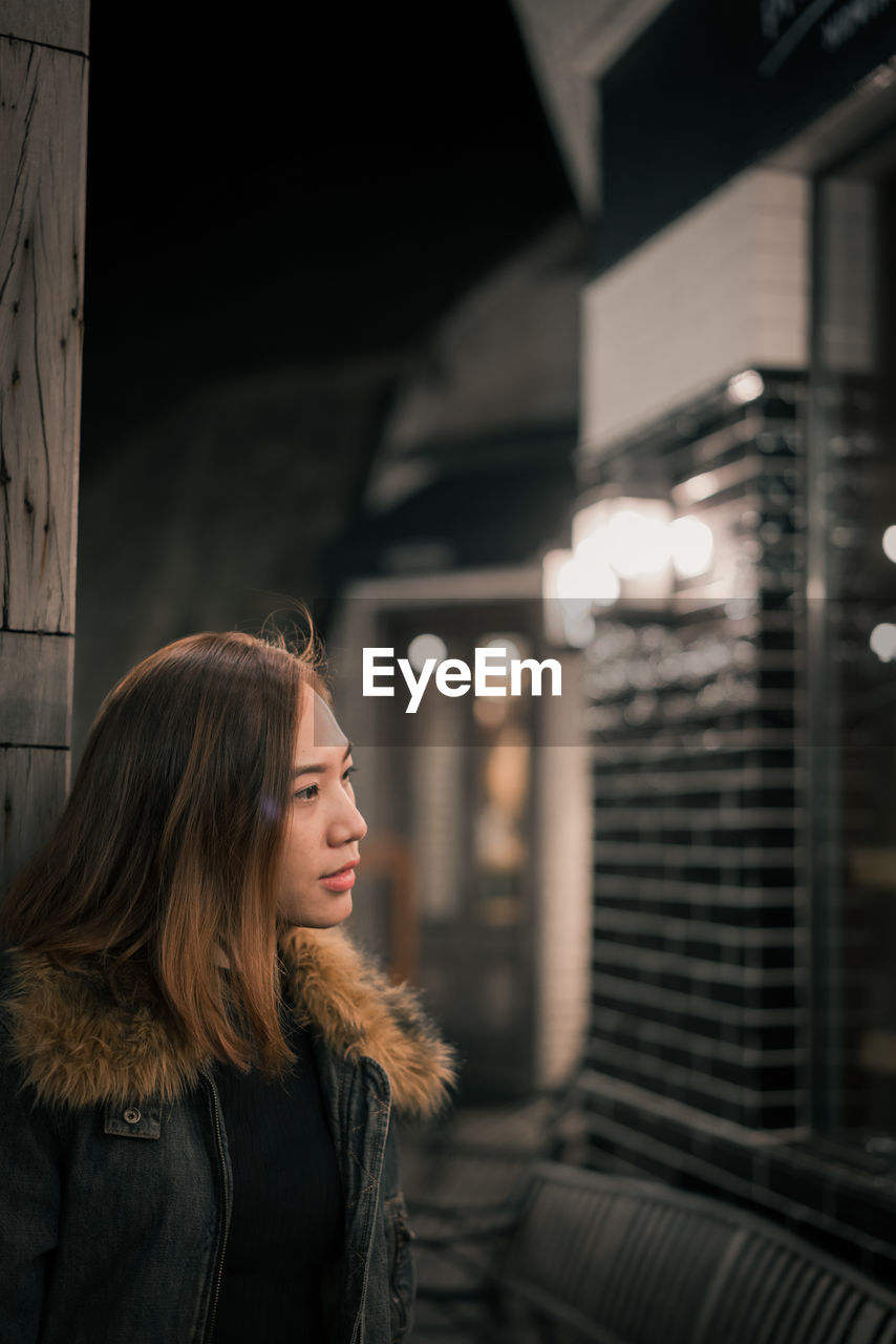 Woman looking away while standing in city at night