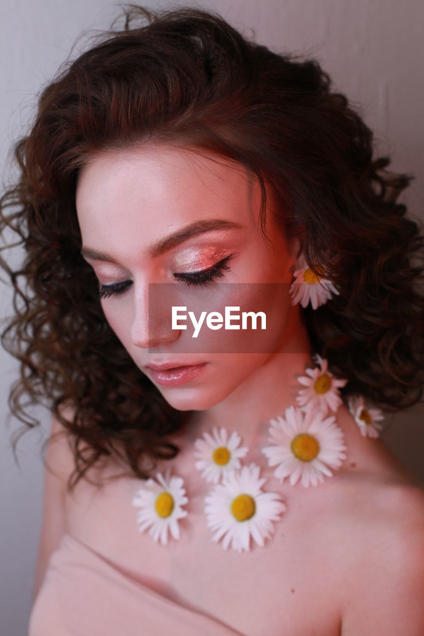 Close-up of teenage girl wearing flowers against wall