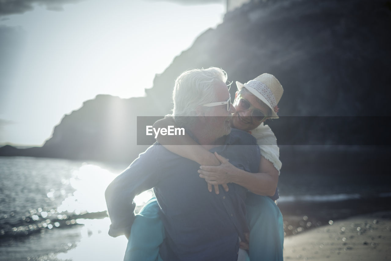 Senior man giving piggy back ride to woman at beach