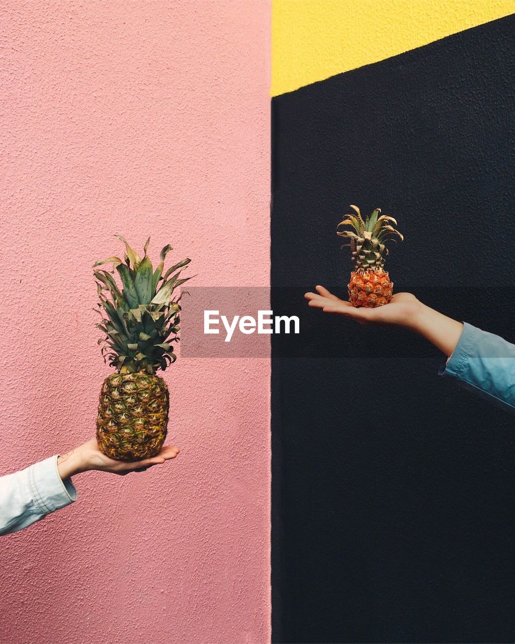 Two people holding pineapples against multi colored wall