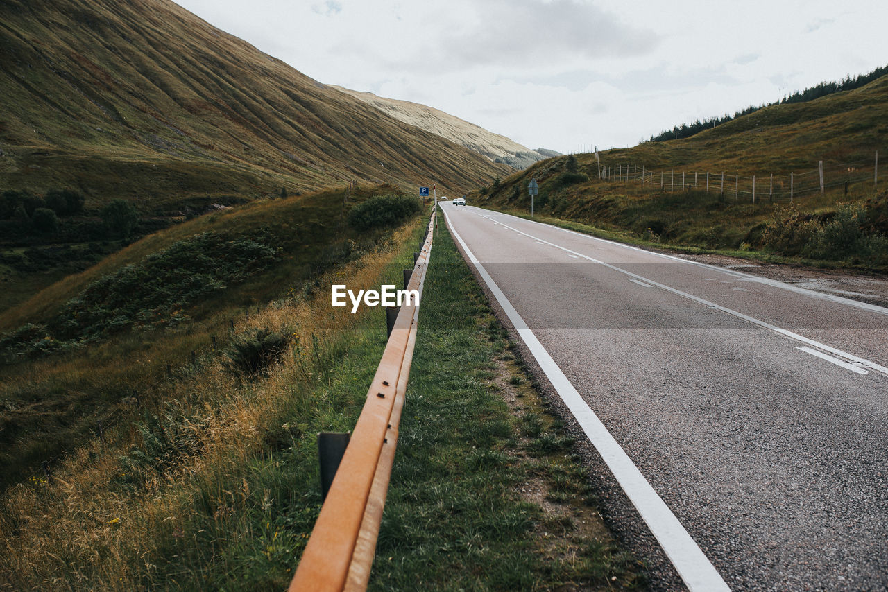 Empty road leading towards mountains against sky