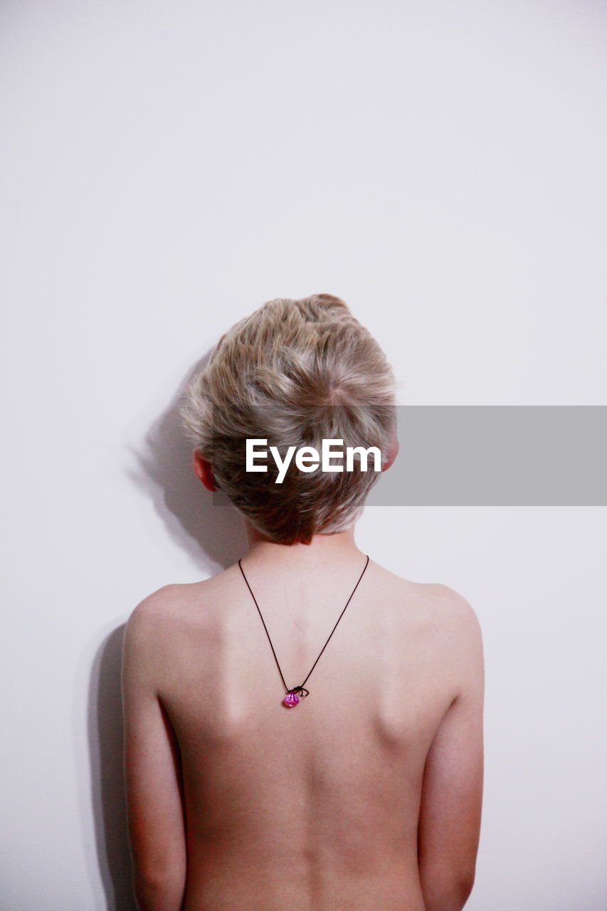 Rear view of shirtless boy wearing pendant against white background
