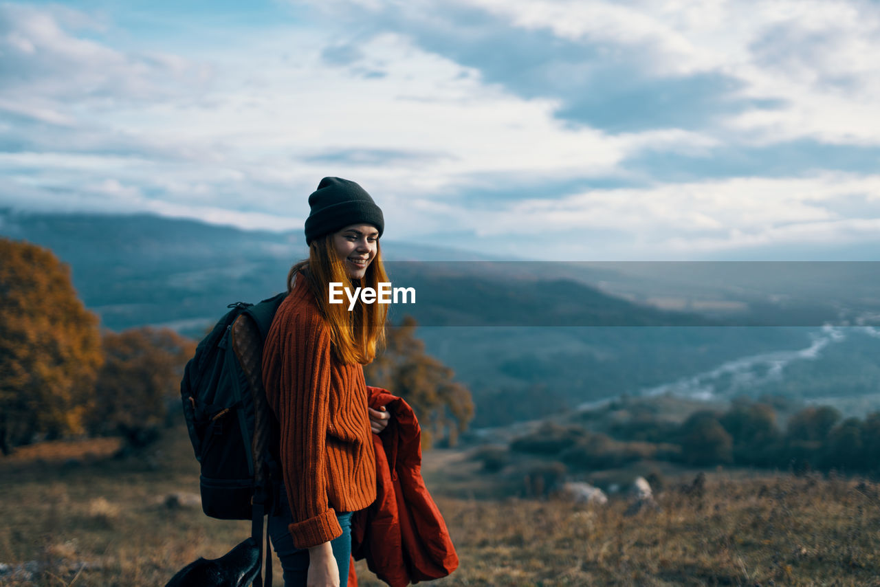 YOUNG WOMAN STANDING AGAINST MOUNTAIN