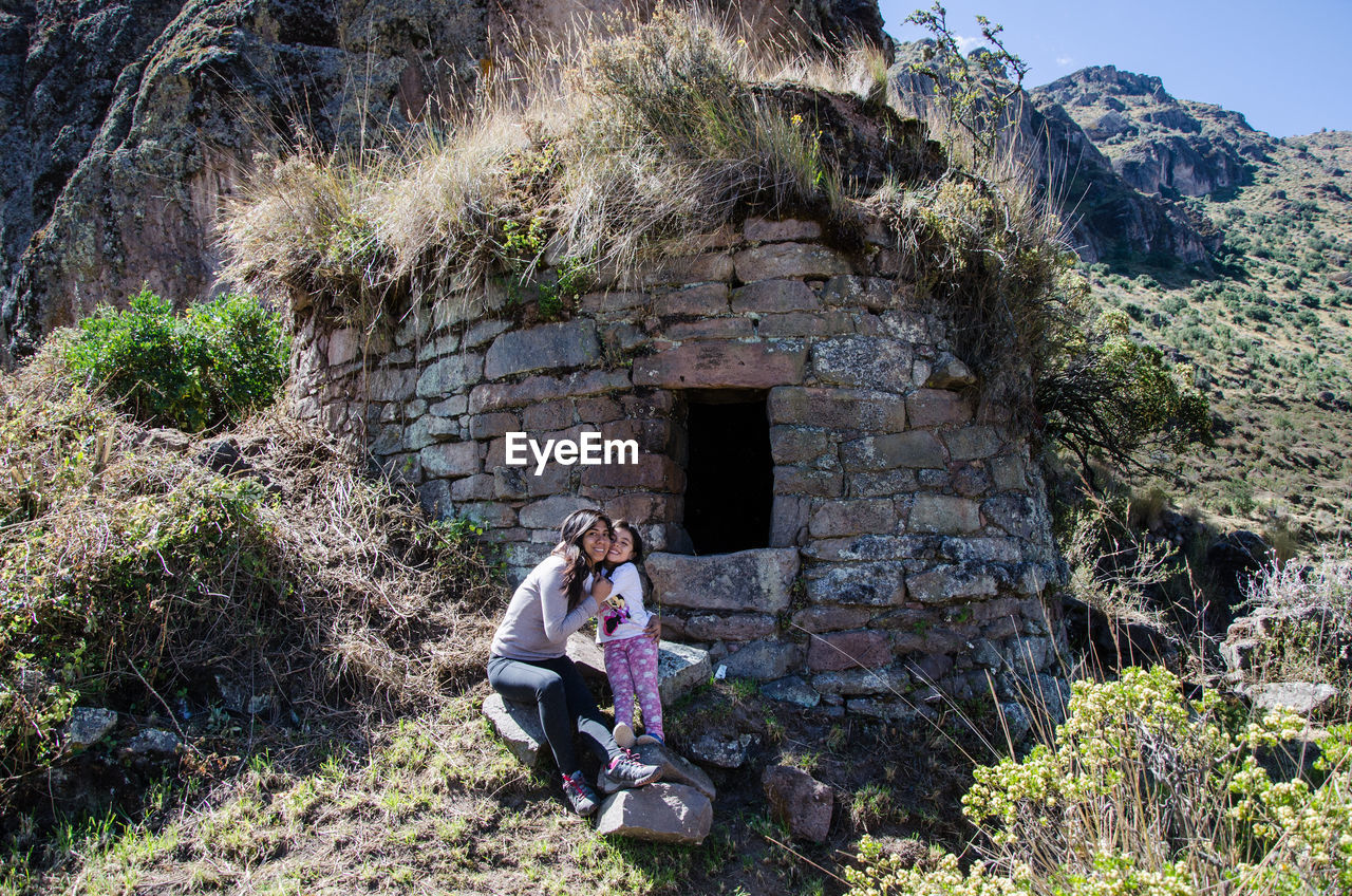 Mother with daughter sitting on rock against built structure