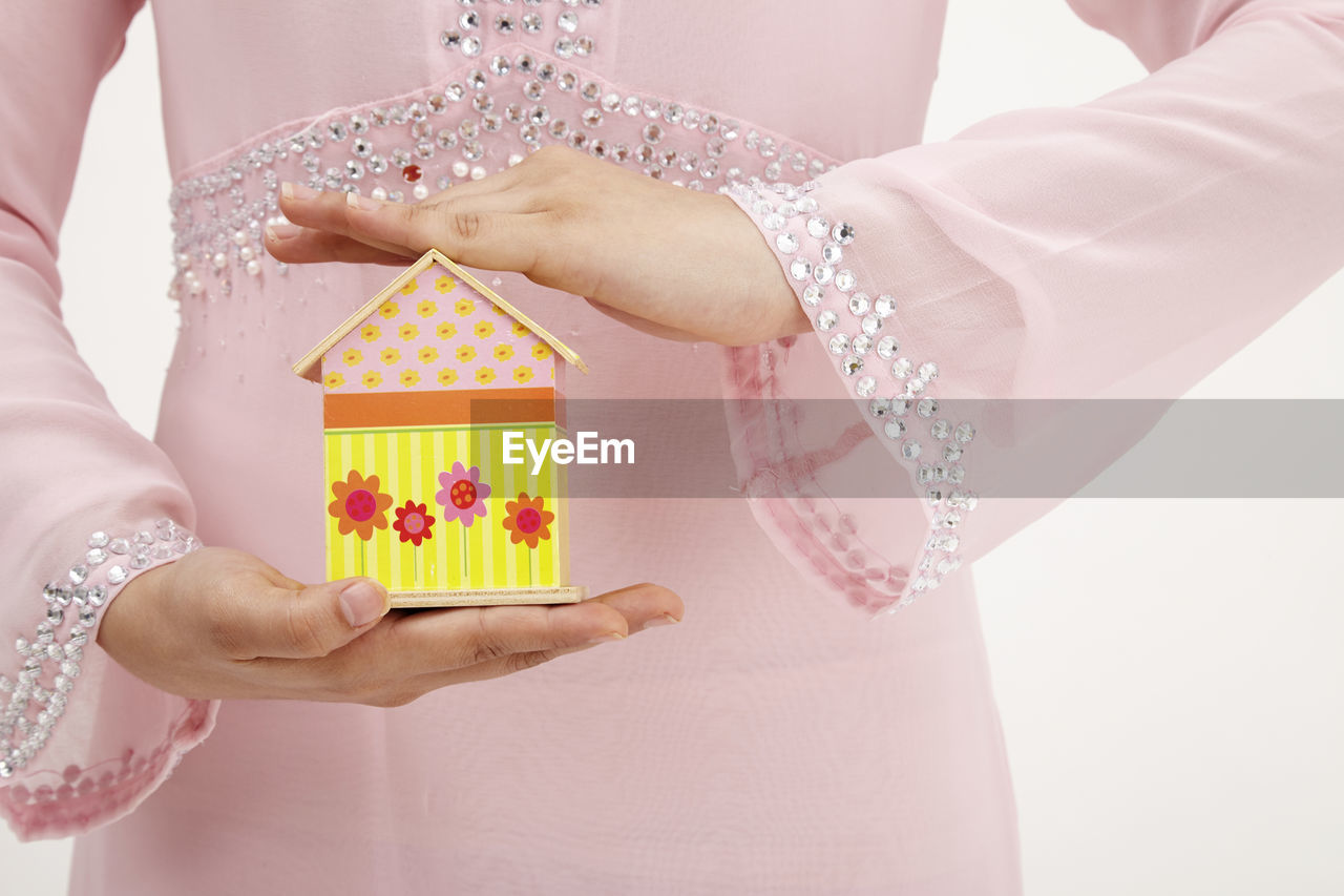 Midsection of woman holding model home against white background