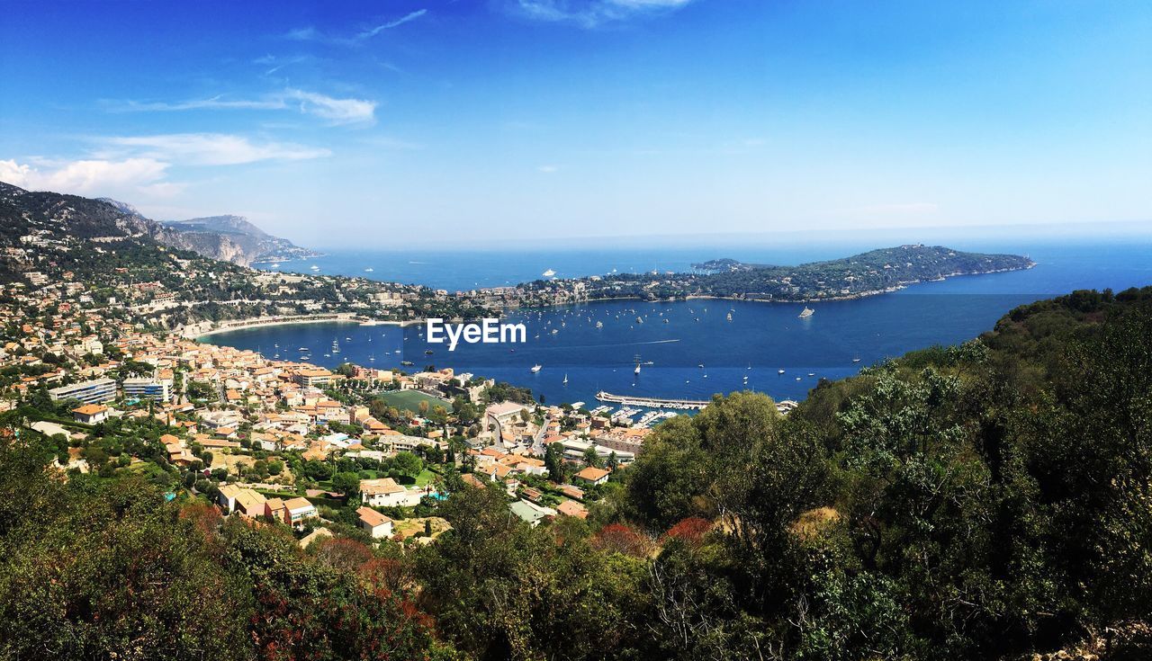 High angle view of city by sea against blue sky