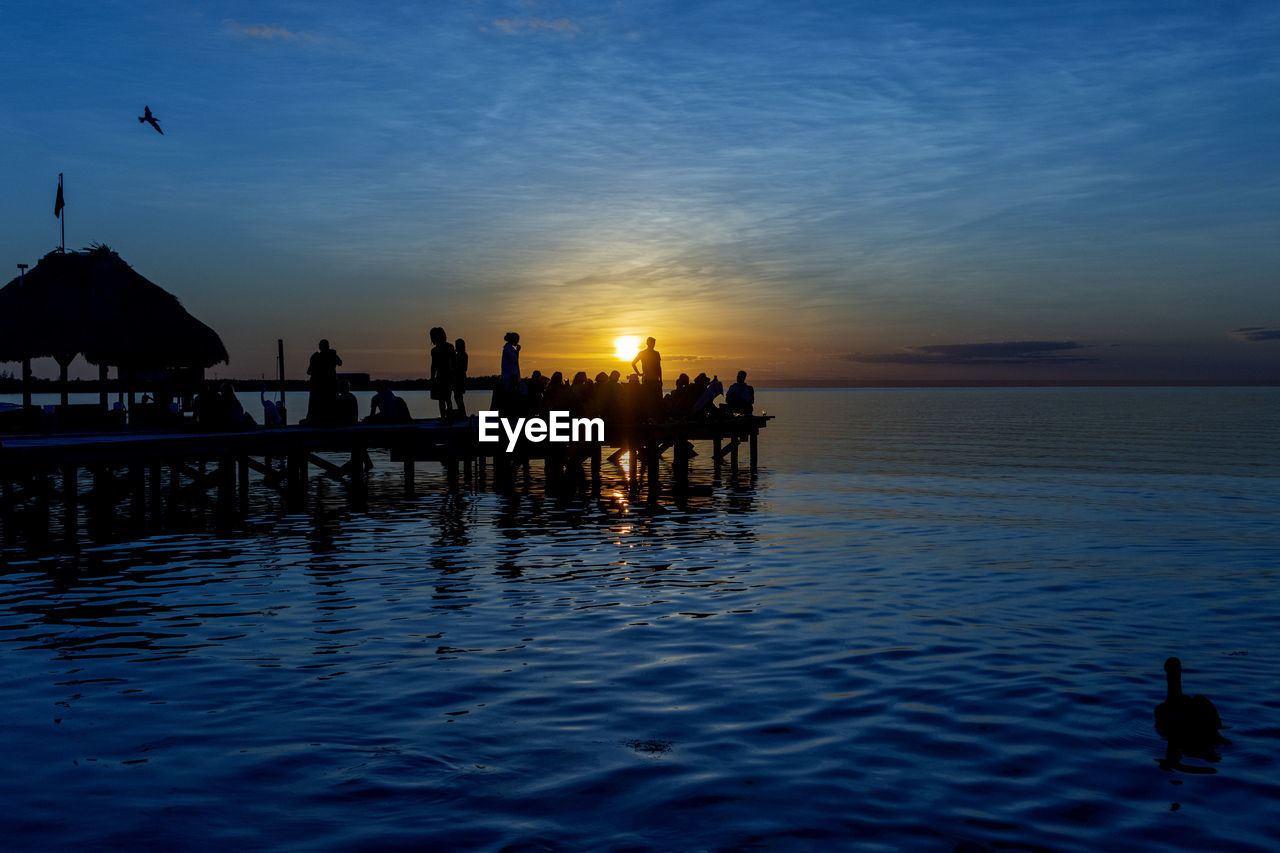 Silhouette people in sea against sky during sunset