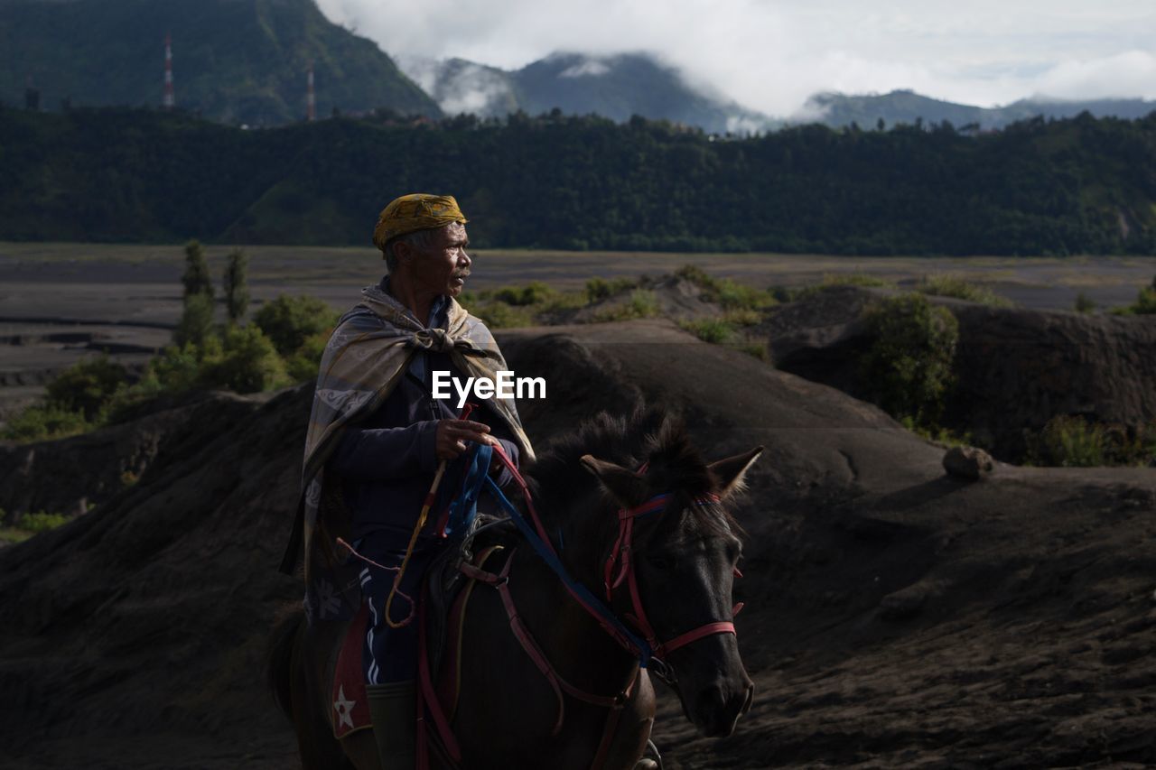 Man looking away while riding horse against landscape 