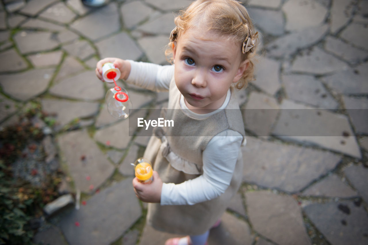 Portrait of cute girl holding bubble wand on footpath