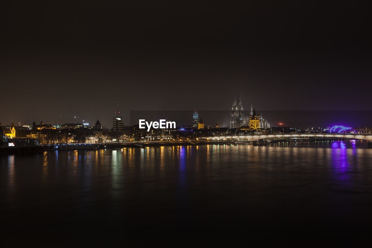 Illuminated cityscape by river at night