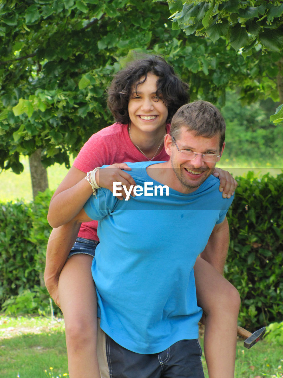 Portrait of smiling man giving piggy back to daughter at park