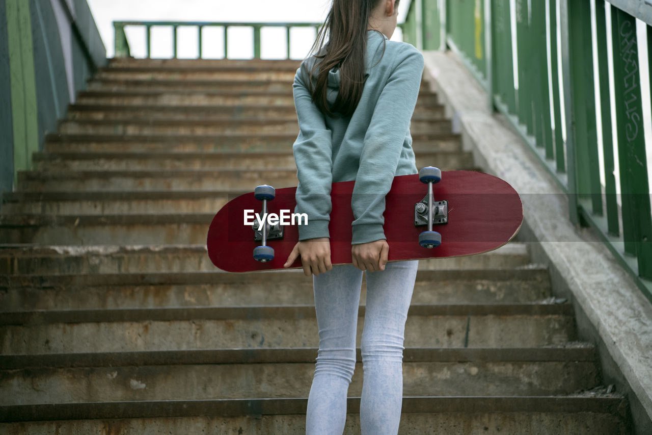Rear view of girl with skateboard standing on steps