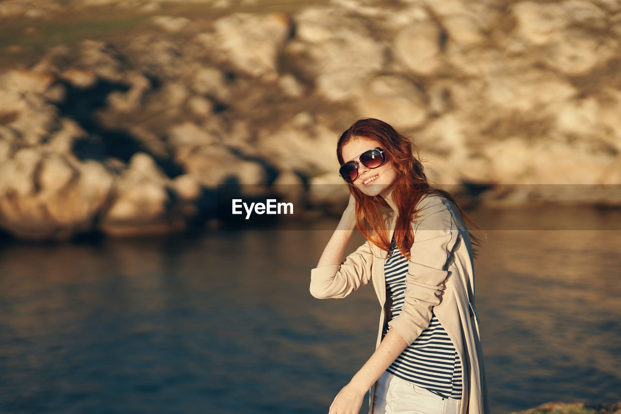 Smiling woman wearing sunglasses standing against water