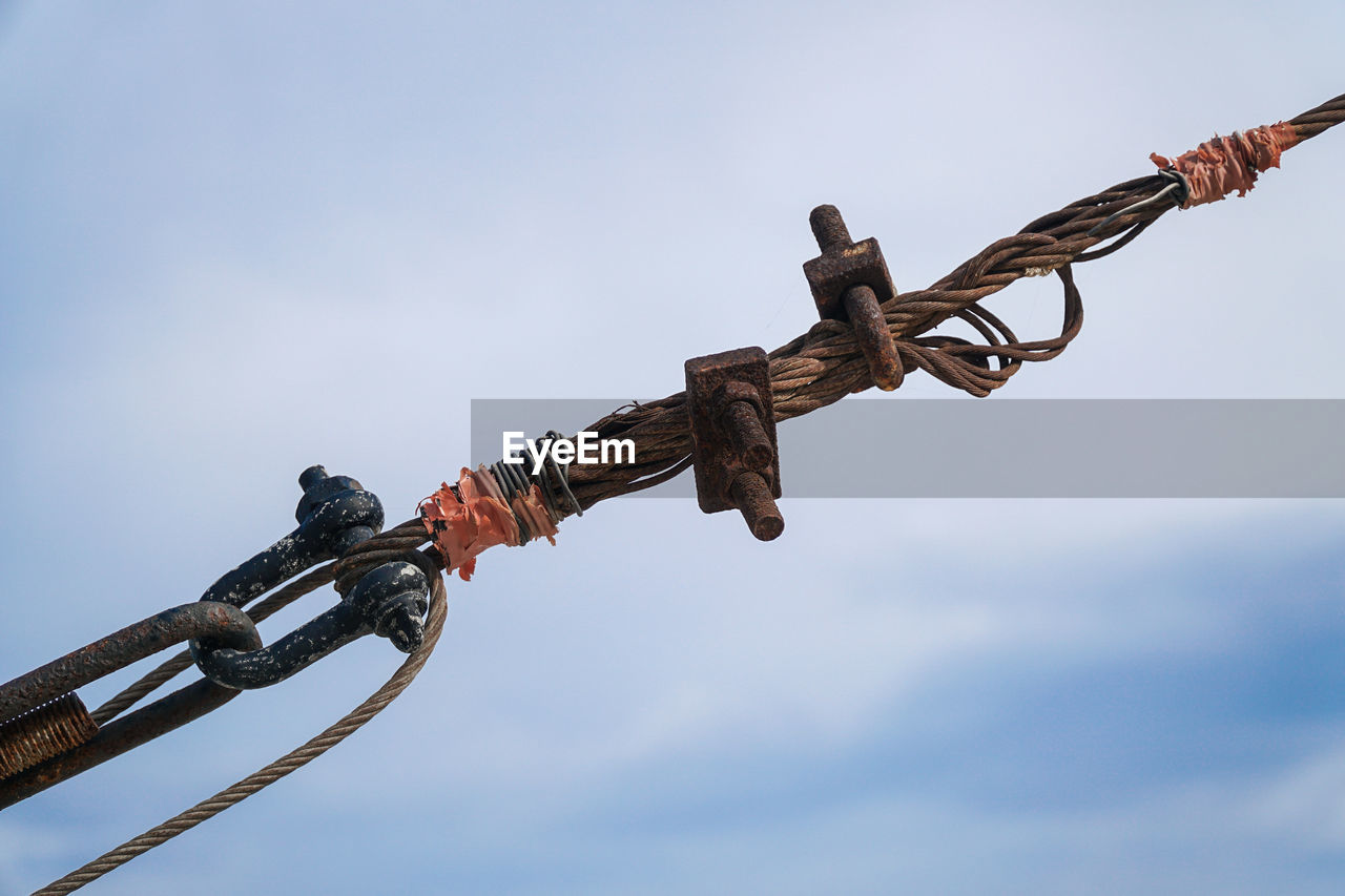 Low angle view of rope tied up on chain against sky