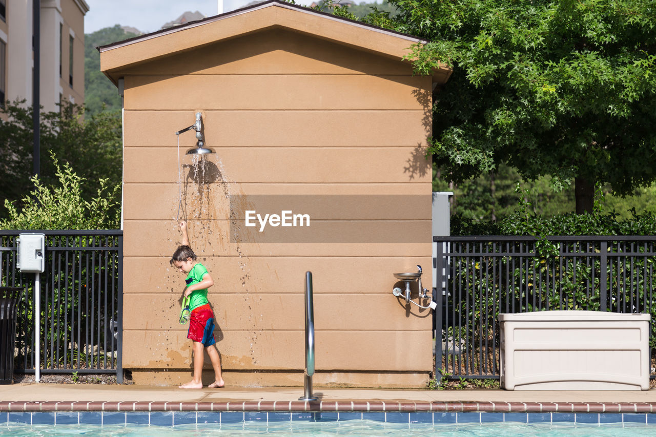 Full length of boy enjoying shower while standing on poolside