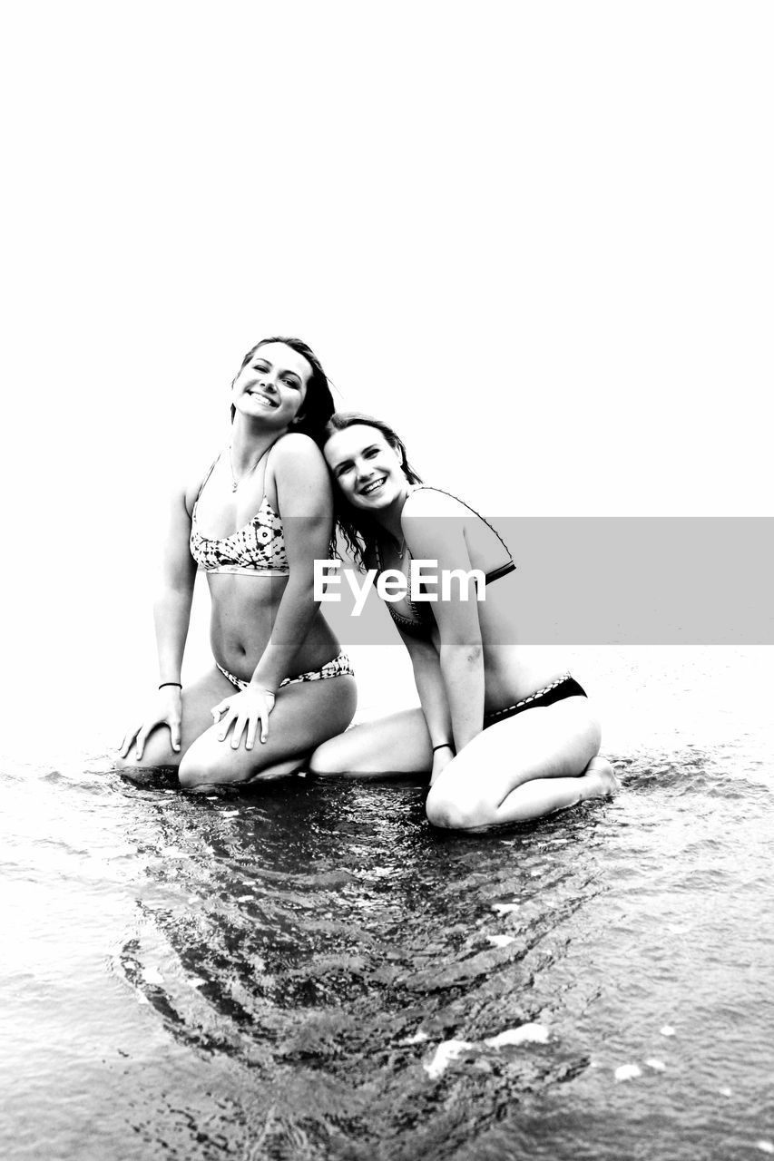 Portrait of female friends in bikini kneeling at beach