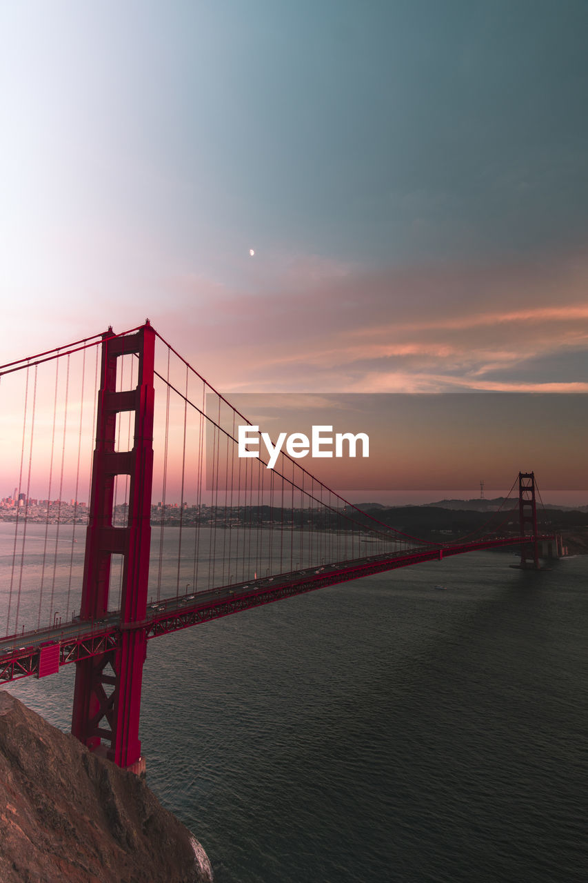 Suspension bridge over sea against sky during sunset