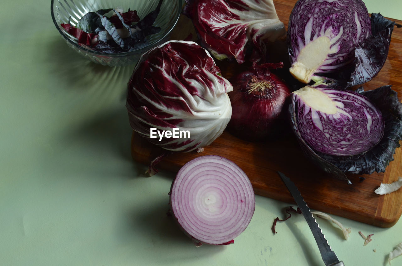 Radicchio, knife, cut red cabbage, red onion, on bamboo cutting board on light green surface