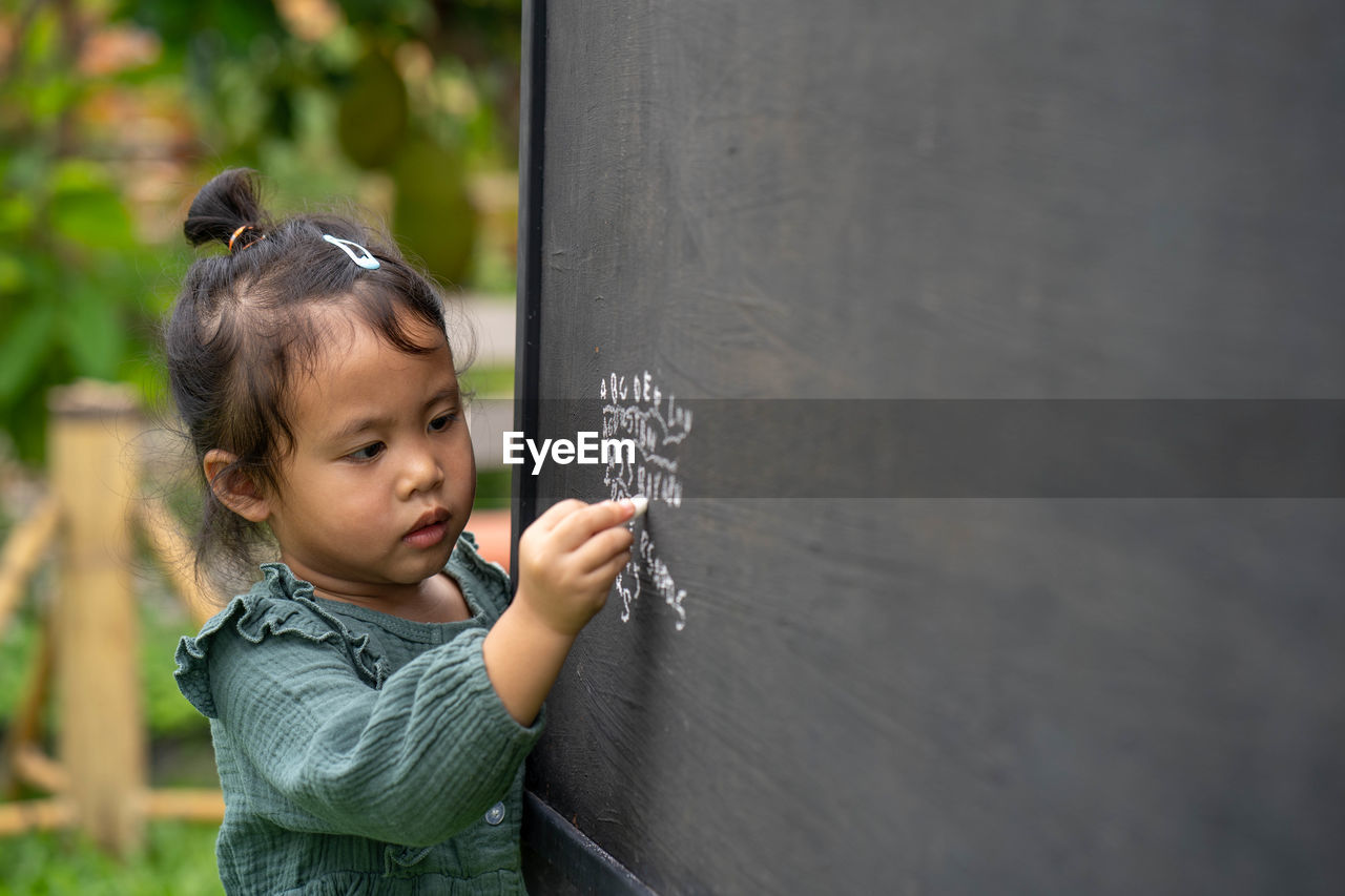 Portrait of cute girl writing alphabet on blackboard