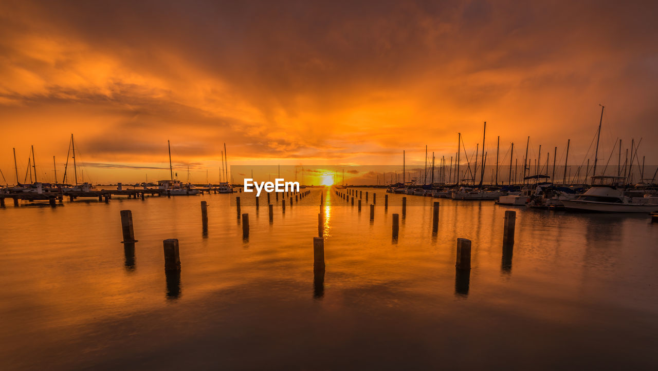 Sailboats moored at harbor against sky during sunset