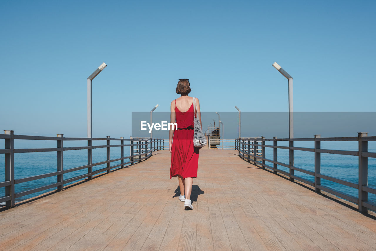 FULL LENGTH REAR VIEW OF WOMAN STANDING ON PIER