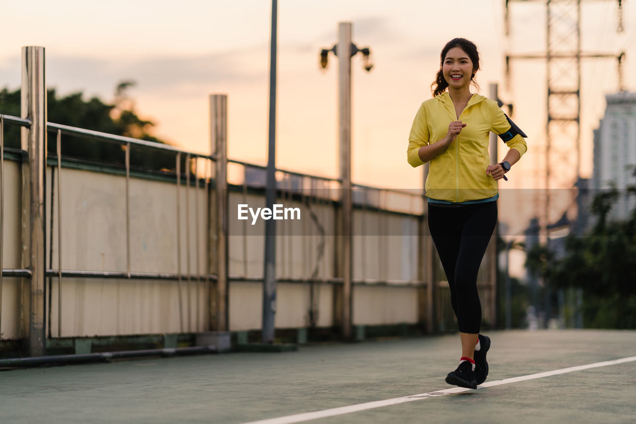 Full length of woman jogging on road in city during sunset