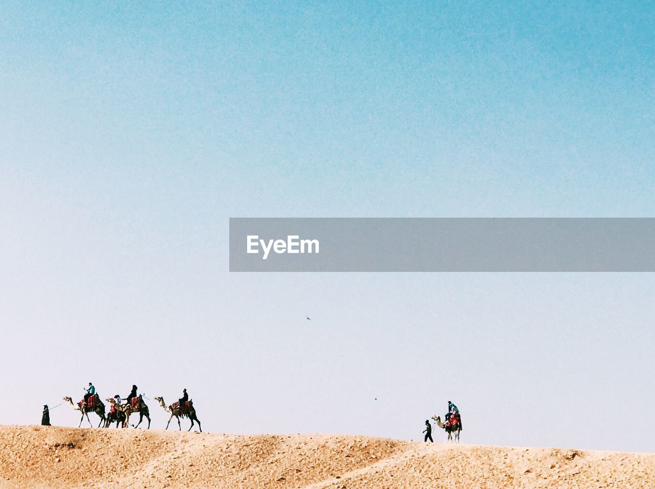 People on sand dune in desert against clear sky