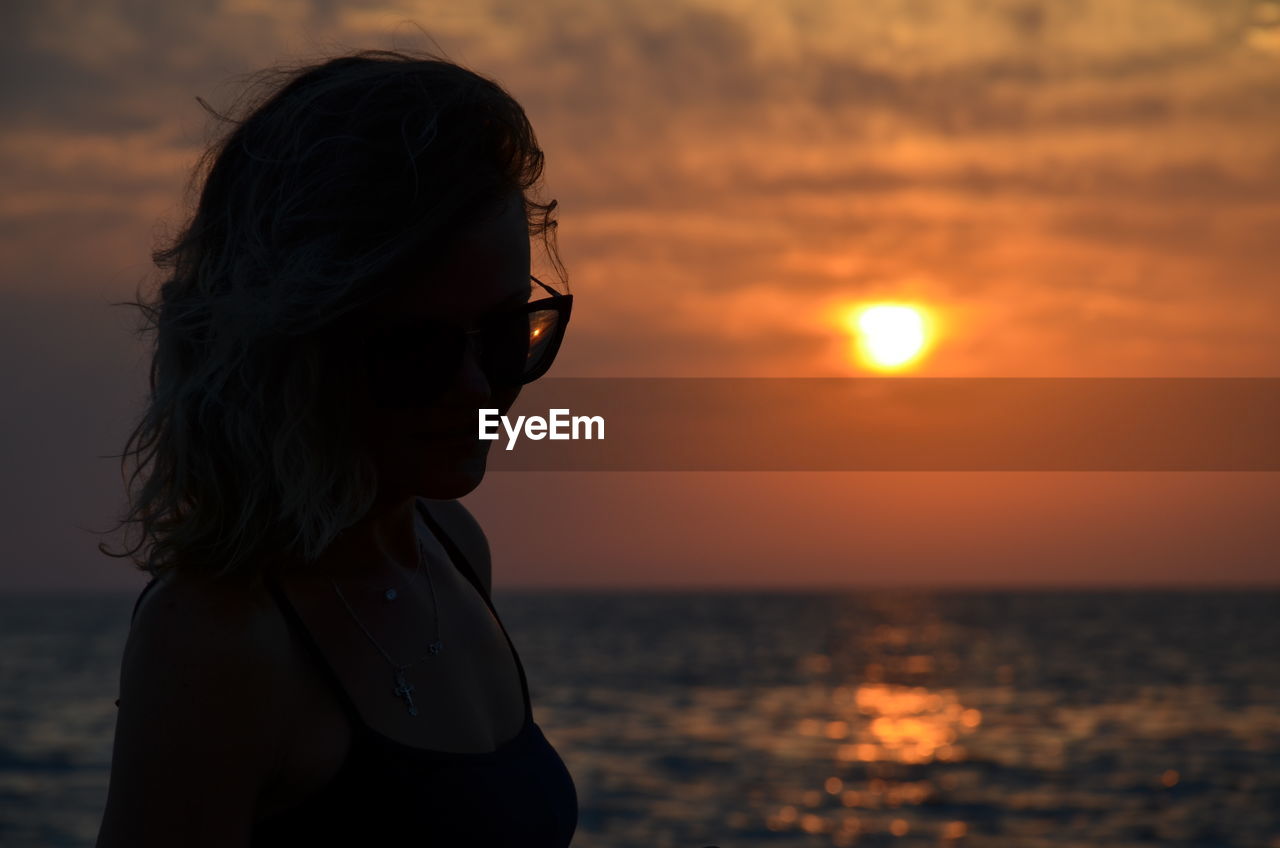 Woman looking at sea against sky during sunset