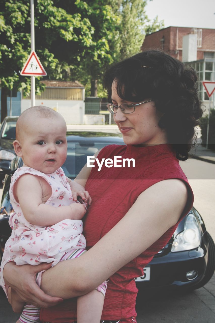 Mother carrying baby girl against car on street