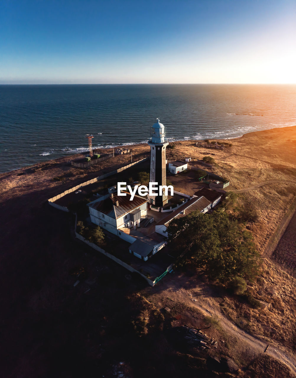 Aerial view of the lighthouse and adjacent technical buildings on the seashore at sunset