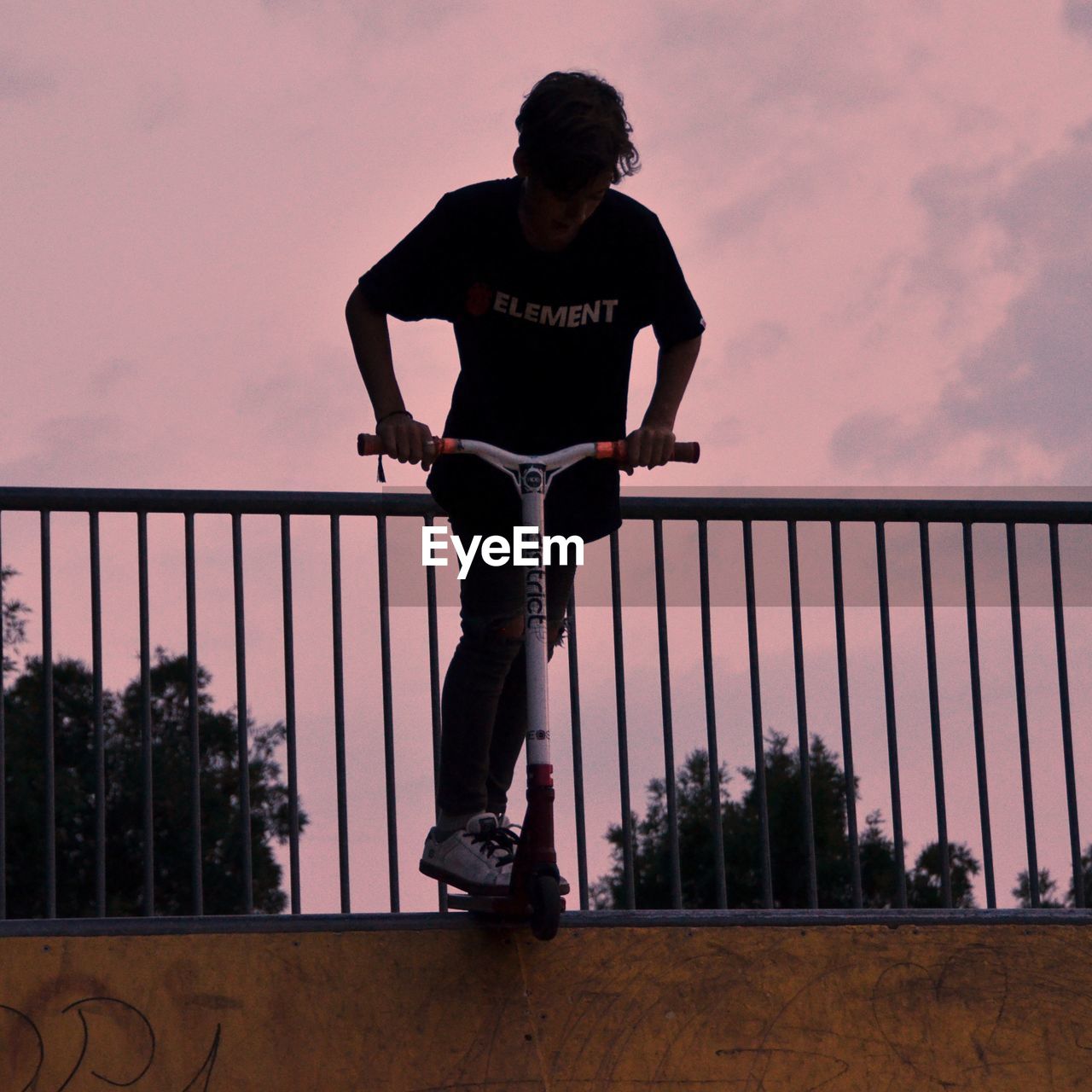 FULL LENGTH OF MAN STANDING AGAINST RAILING AT SUNSET