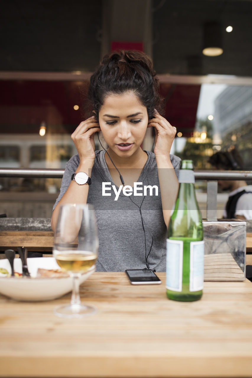 Woman wearing headphones while listening music from mobile phone at sidewalk cafe table