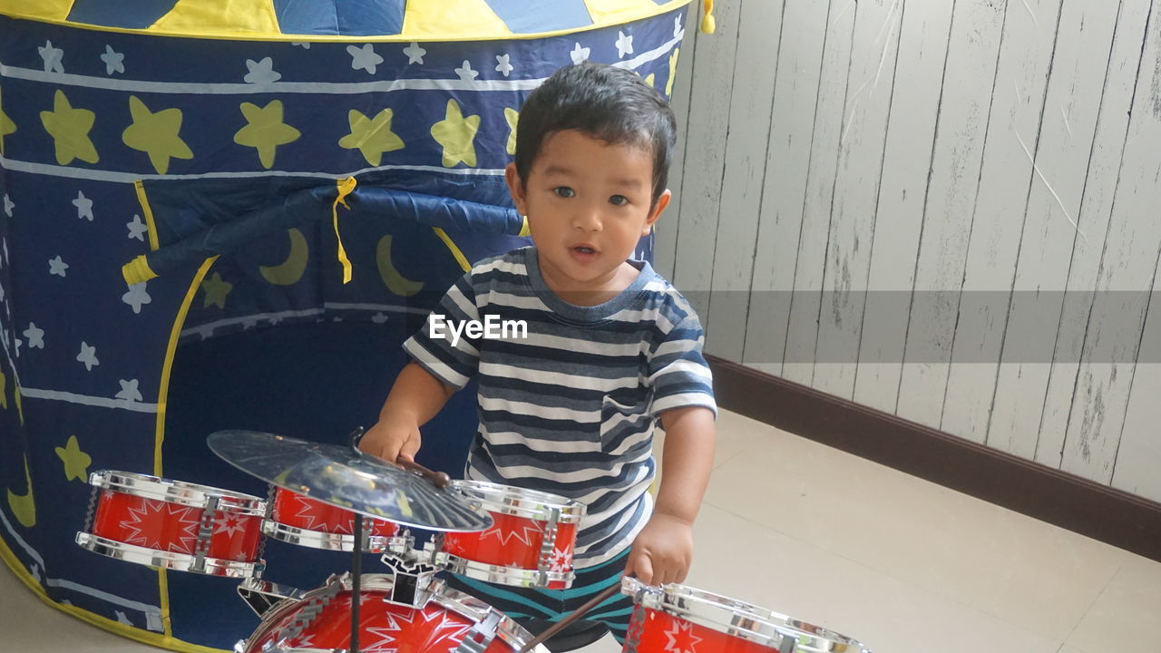 Cute boy playing drums at home