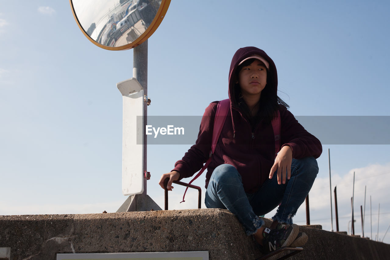 LOW ANGLE VIEW OF WOMAN SITTING AGAINST SKY