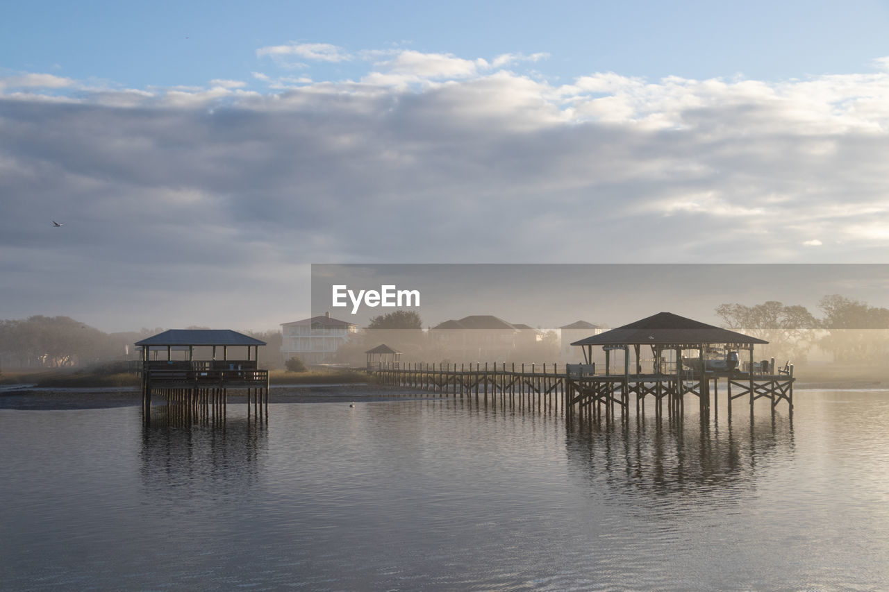 Wooden pier with boat lifts on a river in the morning fog