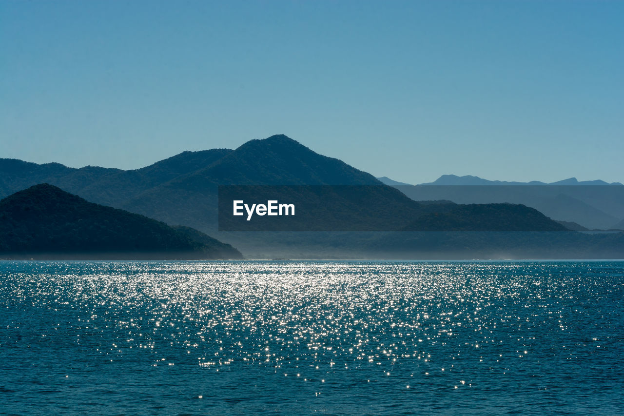 Scenic view of sea and mountains against clear blue sky