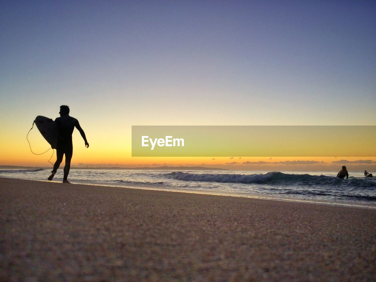 Low angle view of silhouette man with surfboard standing on beach