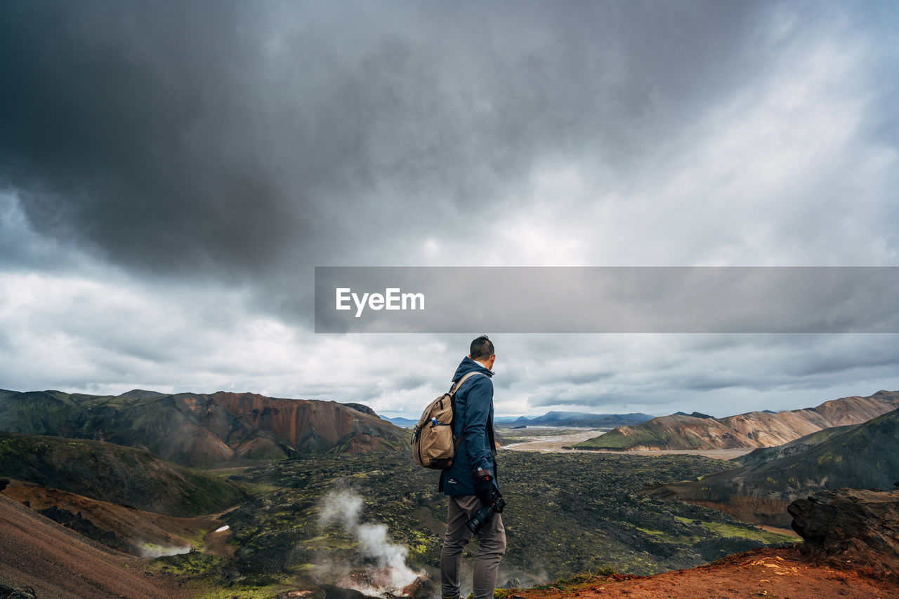 Hiker looking at landscape against cloudy sky