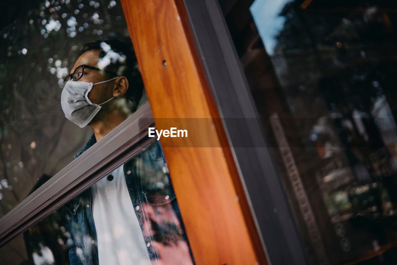 Man wearing mask looking away through glass window