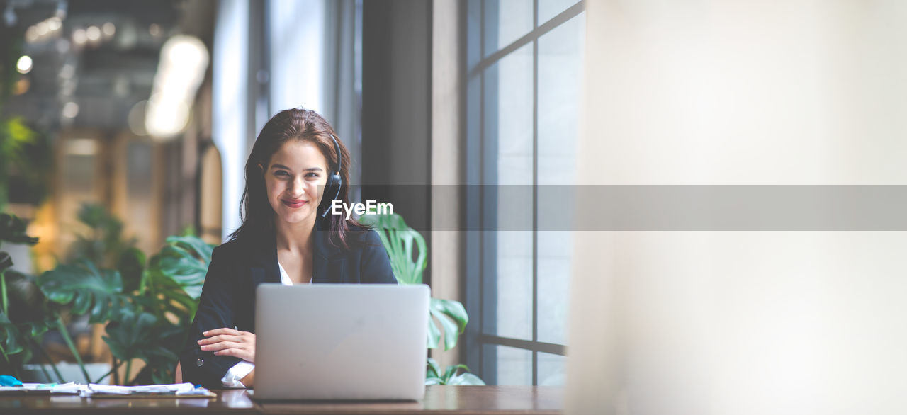 YOUNG WOMAN USING MOBILE PHONE WHILE SITTING ON LAPTOP