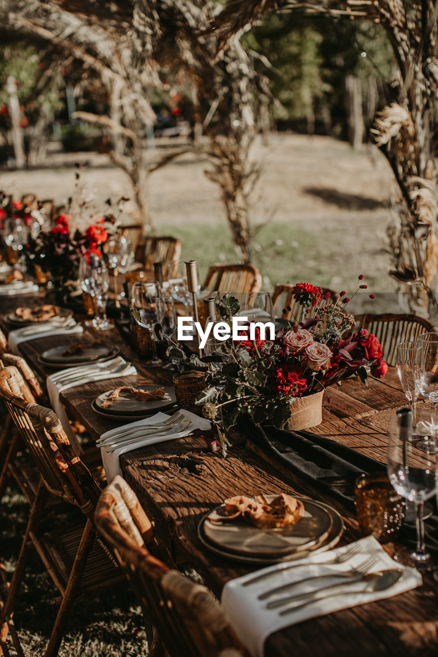 Wooden table served with plates and decorated with flowers in garden for wedding party